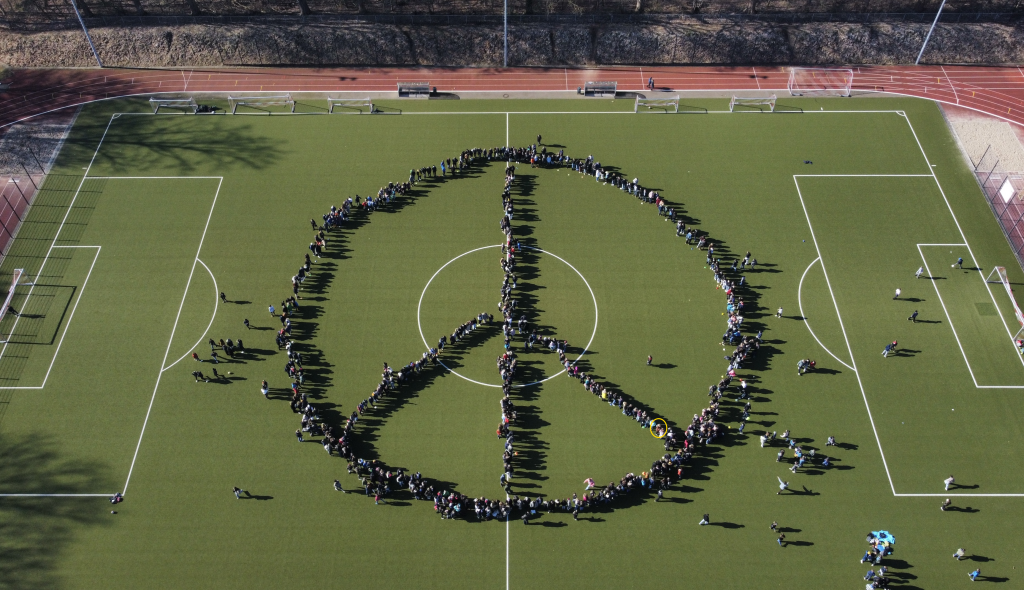 Schülerinnen und Schüler des Walddörfer Gymnasiums bilden auf dem Sportplatz das Peace-Symbol nach.